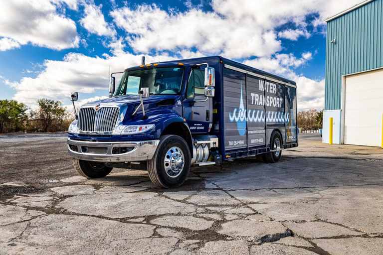 Water Transport box truck parked beside a teal metal building with bay doors